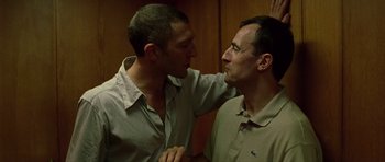 Movie still from “Irreversible” (2002), directed by Gaspar Noé – Two men are touching each other's faces in a room; Medium shot, Low angle