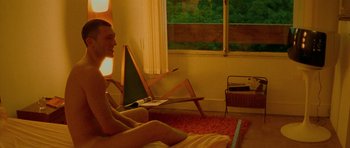 Movie still from “Irreversible” (2002), directed by Gaspar Noé – A man sitting on a bed in front of an open laptop computer; Medium shot, High angle