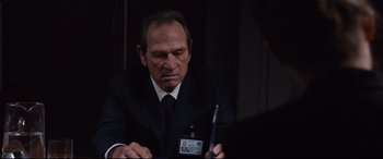 Movie still from “Jason Bourne” (2016), directed by Paul Greengrass – A man in a suit and tie holding a pen; Close Up shot, Over the shoulder angle