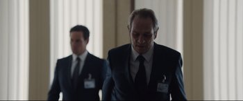 Movie still from “Jason Bourne” (2016), directed by Paul Greengrass – A man in a suit and tie standing next to another man in a suit and tie; Medium shot, Over the shoulder angle