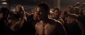 Movie still from “Jason Bourne” (2016), directed by Paul Greengrass – A shirtless man in the middle of a group of people; Medium shot, Over the shoulder angle