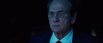 Movie still from “Jason Bourne” (2016), directed by Paul Greengrass – An older man wearing glasses and a suit; Close Up shot, Over the shoulder angle