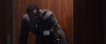 Movie still from “Jason Bourne” (2016), directed by Paul Greengrass – A man in a suit and tie leaning against a wall; Medium shot, Over the shoulder angle