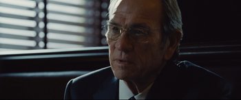 Movie still from “Jason Bourne” (2016), directed by Paul Greengrass – An older man wearing glasses and a suit and tie; Close Up shot, Over the shoulder angle