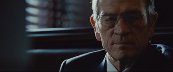 Movie still from “Jason Bourne” (2016), directed by Paul Greengrass – An older man wearing glasses and a suit and tie; Close Up shot, Over the shoulder angle