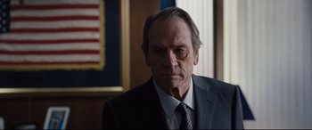 Movie still from “Jason Bourne” (2016), directed by Paul Greengrass – An older man wearing a suit and tie in an office setting; Close Up shot, Low angle