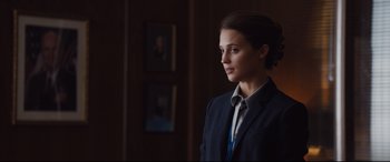 Movie still from “Jason Bourne” (2016), directed by Paul Greengrass – A woman wearing a suit and tie standing in a room; Close Up shot, Over the shoulder angle