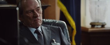 Movie still from “Jason Bourne” (2016), directed by Paul Greengrass – An older man wearing a suit and tie sitting in an office chair; Close Up shot, Over the shoulder angle