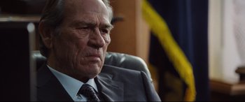 Movie still from “Jason Bourne” (2016), directed by Paul Greengrass – An older man wearing a suit and tie sitting in a chair; Close Up shot, Over the shoulder angle