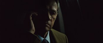 Movie still from “Jason Bourne” (2016), directed by Paul Greengrass – An older man in a suit and glasses talking on a cell phone; Close Up shot, Low angle