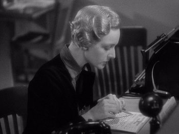 Movie still from “It Happened One Night” (1934), directed by Frank Capra – A woman sitting at a desk working on a computer; Medium shot, High angle