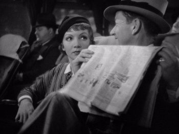 Movie still from “It Happened One Night” (1934), directed by Frank Capra – A woman sitting next to a man holding a newspaper; Close Up shot, High angle