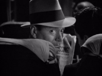 Movie still from “It Happened One Night” (1934), directed by Frank Capra – A black and white photo of a man in a fedora holding a newspaper; Close Up shot, Over the shoulder angle