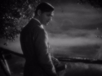 Movie still from “It Happened One Night” (1934), directed by Frank Capra – A black and white photo of a man standing in front of a tree; Medium shot, Over the shoulder angle