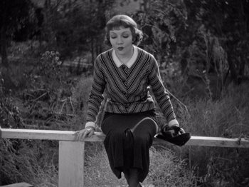 Movie still from “It Happened One Night” (1934), directed by Frank Capra – A woman sitting on a rail in the grass; Medium shot, High angle