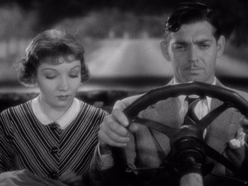 Movie still from “It Happened One Night” (1934), directed by Frank Capra – A man and a woman sitting in a car in front of a steering wheel; Close Up shot, High angle