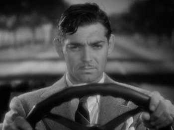 Movie still from “It Happened One Night” (1934), directed by Frank Capra – A black and white photo of a man driving a car; Close Up shot, High angle