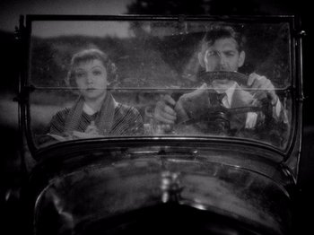 Movie still from “It Happened One Night” (1934), directed by Frank Capra – A man and a woman driving a car in the back of a car; Medium shot, High angle