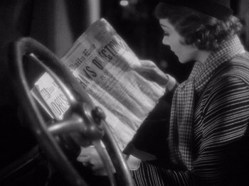 Movie still from “It Happened One Night” (1934), directed by Frank Capra – A woman is reading a newspaper in front of a steering wheel; Close Up shot, Low angle