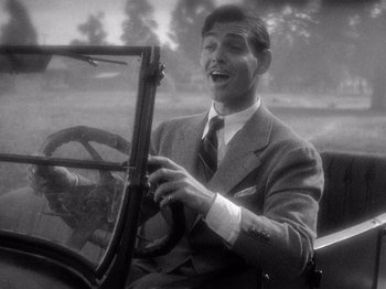 Movie still from “It Happened One Night” (1934), directed by Frank Capra – An old photo of a man in a suit driving a car; Medium shot, High angle