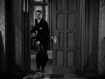 Movie still from “It Happened One Night” (1934), directed by Frank Capra – A black and white photo of a man standing in a doorway; Medium shot, High angle