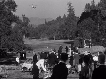 Movie still from “It Happened One Night” (1934), directed by Frank Capra – A group of people standing in a field with a plane in the background; Extreme Wide shot, High angle