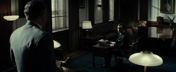 Movie still from “J. Edgar” (2011), directed by Clint Eastwood – A man sitting at a table in a living room; Wide shot, Over the shoulder angle