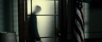Movie still from “J. Edgar” (2011), directed by Clint Eastwood – A person standing in front of a frosted glass door; Medium shot, Low angle