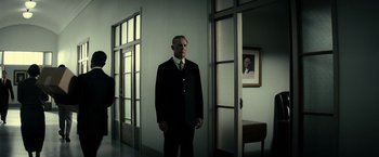 Movie still from “J. Edgar” (2011), directed by Clint Eastwood – A man in a suit standing in front of a door way; Wide shot, Low angle