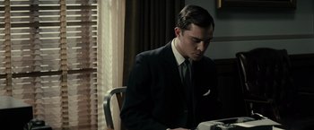 Movie still from “J. Edgar” (2011), directed by Clint Eastwood – A man in a suit and tie sitting at a table; Medium shot, Low angle