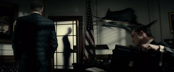 Movie still from “J. Edgar” (2011), directed by Clint Eastwood – A man standing in front of an american flag in a room; Wide shot, Low angle