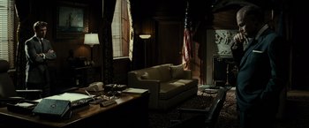 Movie still from “J. Edgar” (2011), directed by Clint Eastwood – A living room filled with furniture next to an american flag; Wide shot, High angle