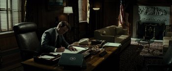 Movie still from “J. Edgar” (2011), directed by Clint Eastwood – A man sitting at a desk writing on a piece of paper; Wide shot, Low angle