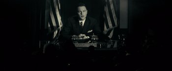 Movie still from “J. Edgar” (2011), directed by Clint Eastwood – A black and white photo of a man sitting at a desk; Medium shot, Low angle