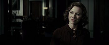 A woman in a brown sweater standing in front of a window