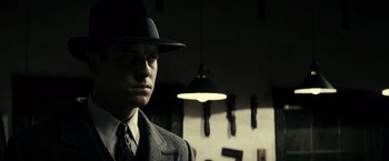 Movie still from “J. Edgar” (2011), directed by Clint Eastwood – A man wearing a suit and a hat in front of a light; Close Up shot, Low angle
