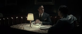 Movie still from “J. Edgar” (2011), directed by Clint Eastwood – A man sitting at a table in front of a lit lamp; Medium shot, Over the shoulder angle