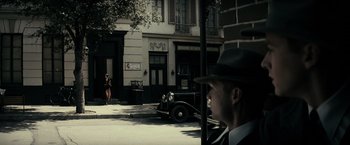 Movie still from “J. Edgar” (2011), directed by Clint Eastwood – A man wearing a hat standing next to a street; Wide shot, Over the shoulder angle