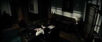 Movie still from “J. Edgar” (2011), directed by Clint Eastwood – A man sitting at a desk writing on a book; Wide shot, High angle