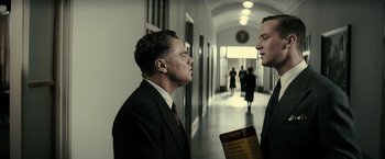 Movie still from “J. Edgar” (2011), directed by Clint Eastwood – Two men in suits are standing in a hallway; Medium shot, Low angle