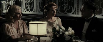Movie still from “J. Edgar” (2011), directed by Clint Eastwood – A woman sitting at a table with flowers in front of a lamp; Medium shot, Over the shoulder angle