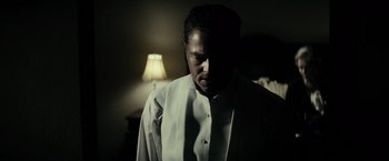 Movie still from “J. Edgar” (2011), directed by Clint Eastwood – A man standing in a dark room next to a lamp; Close Up shot, Low angle