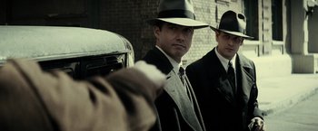 Movie still from “J. Edgar” (2011), directed by Clint Eastwood – A man in a suit and a hat standing next to another man in a suit; Close Up shot, Over the shoulder angle