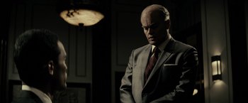 Movie still from “J. Edgar” (2011), directed by Clint Eastwood – A man in a suit and tie standing in front of a lamp; Medium shot, Low angle