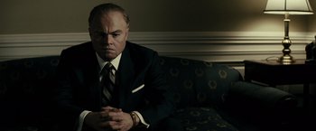 Movie still from “J. Edgar” (2011), directed by Clint Eastwood – A man in a suit sitting on top of a couch; Close Up shot, Low angle