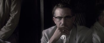 Movie still from “JFK” (1991), directed by Oliver Stone – A person wearing glasses and a suit; Close Up shot, Low angle