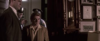 Movie still from “JFK” (1991), directed by Oliver Stone – A man wearing a suit and a hat standing next to another man in a suit; Medium shot, Over the shoulder angle