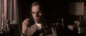 Movie still from “JFK” (1991), directed by Oliver Stone – A man in a suit smoking a pipe; Close Up shot, Low angle