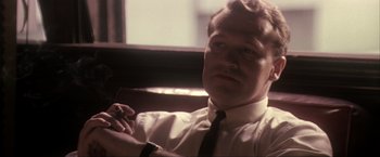 Movie still from “JFK” (1991), directed by Oliver Stone – A man sitting in front of a window with a cigarette in his mouth; Close Up shot, Low angle