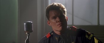 Movie still from “JFK” (1991), directed by Oliver Stone – A man in a military uniform with a microphone in front of him; Close Up shot, Low angle